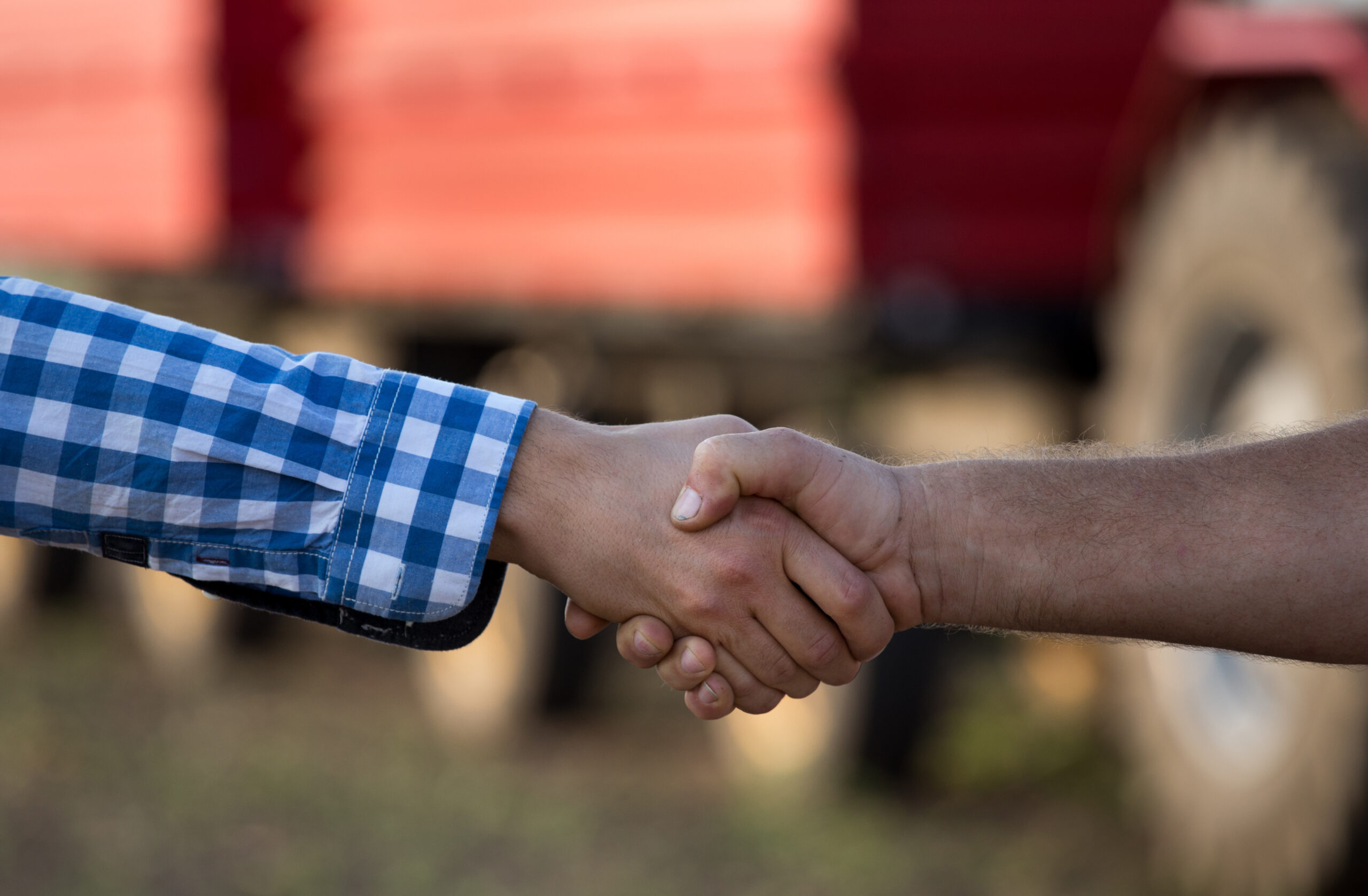 Two farmers shaking hands in field in front of a tractor